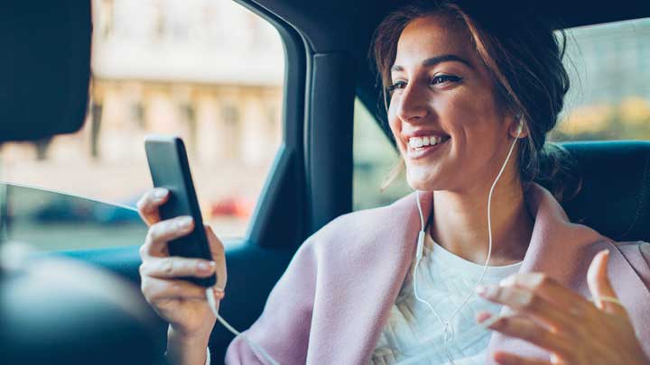 Perempuan dalam mobil menggunakan ponselnya sambil tersenyum