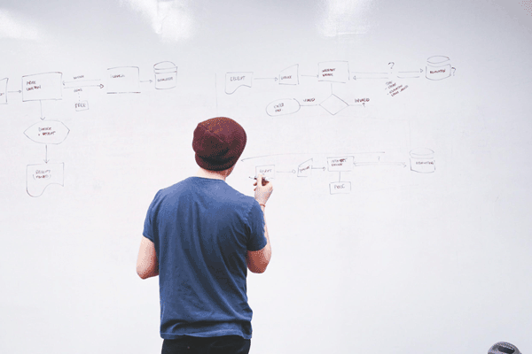 A man facing a whiteboard with writing on it